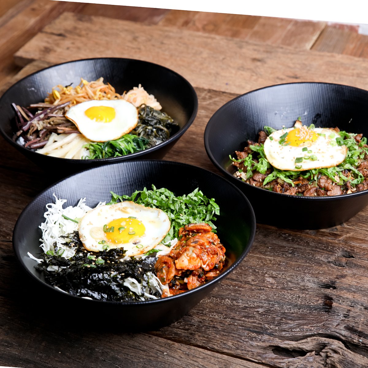 볶음밥 3종 — 검은 그릇, 계란프라이, 나무 테이블