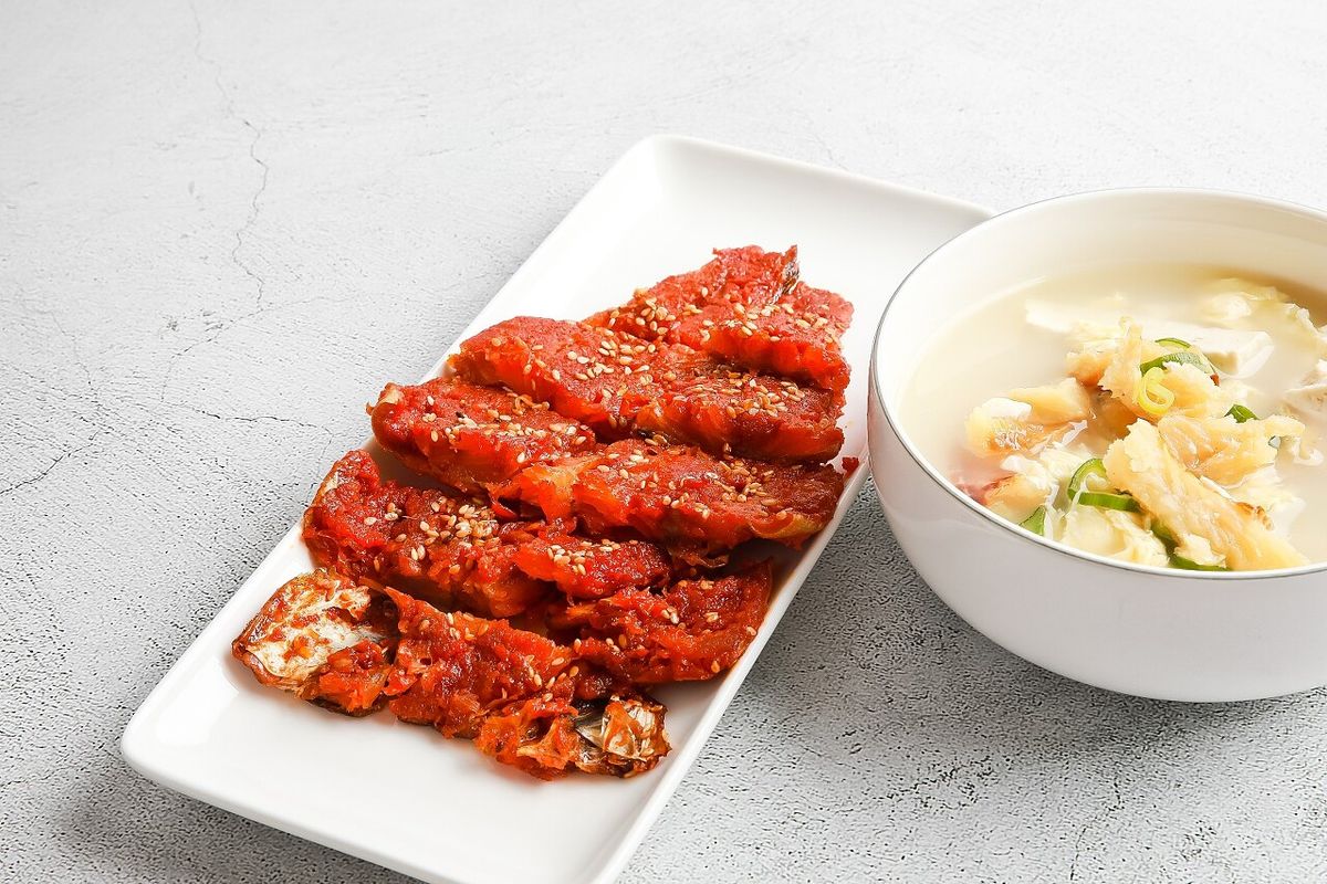 나무 숟가락으로 북엇국을 떠올린 사이드 클로즈업 — 명태 살과 국물이 보임